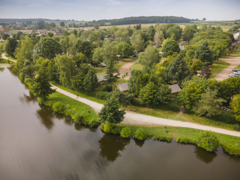 Aerial view of Huttopia Etang de Fouché glamping site in Bourgogne, surrounded by trees and a lake.