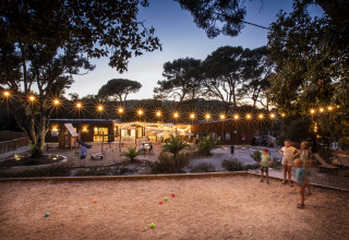 Imagen al atardecer de Huttopia Forêt de Janas - Glamping Côte d’Azur con luces, niños y área de juegos.