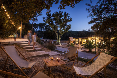 Glamping-Bereich im Huttopia Forêt de Janas mit Lounge-Stühlen, Lichtern und Gästen bei Sonnenuntergang.