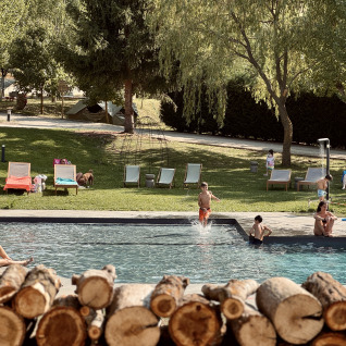 Familier og børn nyder en svømmetur ved Basecamps - Cabins Girona, et glamping-sted med swimmingpool og telte.