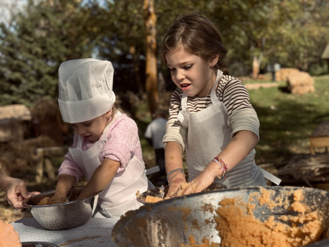 Two kids cooking outdoors at Basecamps - Cabins Girona, wearing aprons and a chef’s hat in nature.