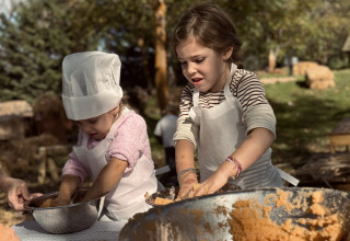 Two kids cooking outdoors at Basecamps - Cabins Girona, wearing aprons and a chef’s hat in nature.