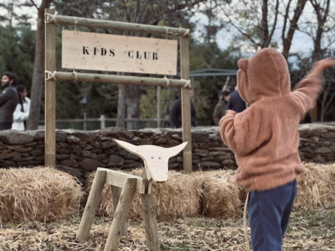 Enfant déguisé en ours jouant au Kids Club de Basecamps - Cabins Girona avec des bottes de foin et un jouet en bois.