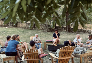 Un grupo de personas sentadas en círculo en sillas de madera al aire libre en Basecamps - Cabins Girona.