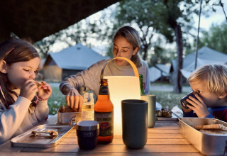 Famille prenant un repas dehors avec lampe lors d’un séjour glamping à Basecamps - Cabins Girona, tentes derrière.
