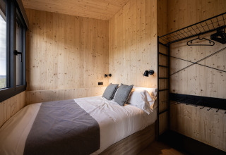 Chambre glamping Basecamps - Cabins Girona avec lit double, murs en bois clair et grande fenêtre sur la nature.