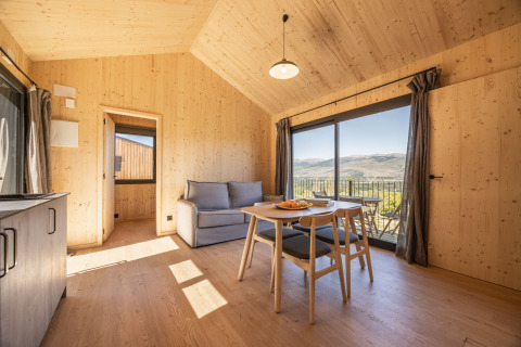 Interno di Basecamps - Cabins Girona glamping, arredo in legno chiaro, vista montagna e balcone.