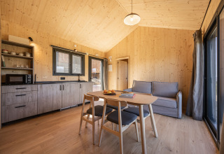 Interno moderno in legno presso Basecamps - Cabins Girona con tavolo da pranzo, divano e angolo cottura.
