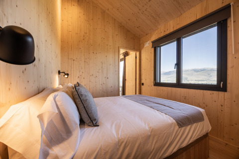 Alojamiento glamping Basecamps - Cabins Girona con habitación de madera, cama doble y vistas montañosas.