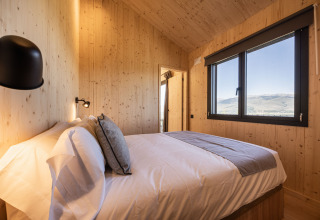 Basecamps - Cabins Girona glamping værelse med trævægge, stor seng og udsigt til bjergene.