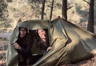 Due donne sorridono davanti alla tenda a Basecamps - Cabins Girona durante la loro esperienza di campeggio.