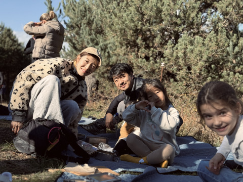 Familie entspannt beim Picknick vor Basecamps - Cabins Girona zwischen sonnenbeschienenen Bäumen.