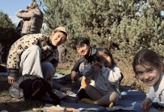 Family enjoys an outdoor picnic at Basecamps - Cabins Girona, surrounded by trees and natural sunlight.