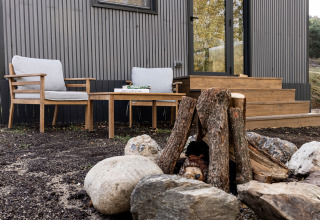 Udendørs siddeområde ved Basecamps - Cabins Girona med træmøbler, pejs og moderne trækabine.