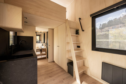 Cabaña glamping Basecamps - Cabins Girona con interior de madera clara, escalera y amplia ventana al exterior.