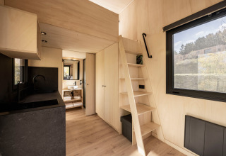 Cabaña glamping Basecamps - Cabins Girona con interior de madera clara, escalera y amplia ventana al exterior.