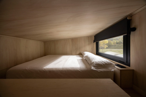 Interieur van Basecamps - Cabins Girona glamping, bed bij raam met natuurzicht in gezellige houten cabine.