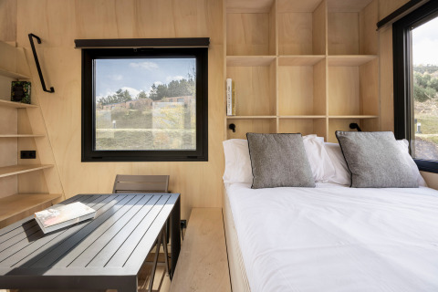 Moderne Basecamps - Cabins Girona glampingaccommodatie met bed, eettafel en grote ramen in het interieur.
