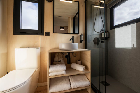 Baño moderno en Basecamps - Cabins Girona con ducha, inodoro, lavabo, toallas limpias y diseño minimalista.