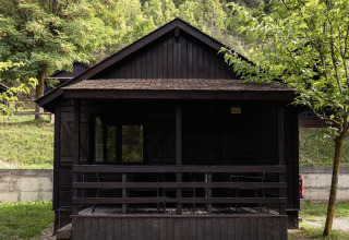 Mørk træhytte med veranda omgivet af grønt, Basecamps - Cabins Girona, glamping- eller campingbolig.