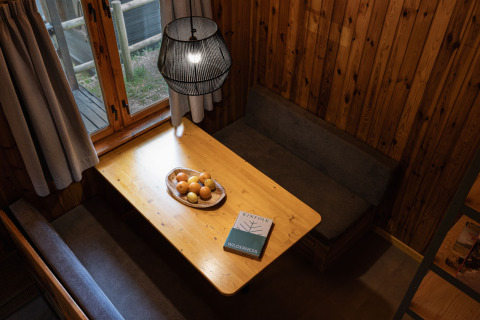 Gezellig eethoekje bij Basecamps - Cabins Girona met houten wanden, tafel, banken, fruitschaal en boek.