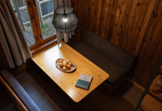 Lyst og hyggeligt hjørne i Basecamps - Cabins Girona med trævægge, spisebord, frugtskål og bog.
