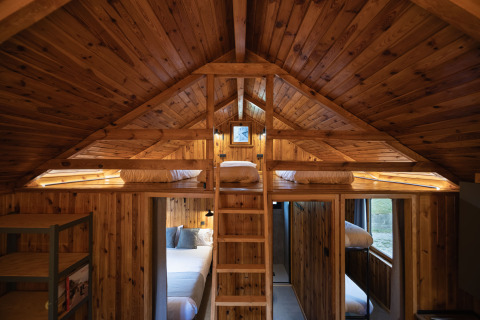 Cabaña de madera interior con camas tipo loft, escalera y luz cálida en Basecamps - Cabins Girona, glamping.