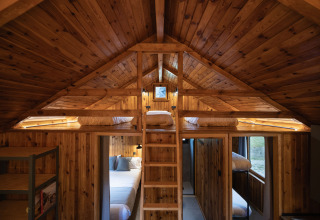 Cabaña de madera interior con camas tipo loft, escalera y luz cálida en Basecamps - Cabins Girona, glamping.