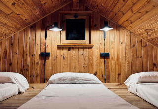 Acogedora cabaña de madera con tres camas y techo inclinado, Basecamps - Cabins Girona, ideal para glamping.