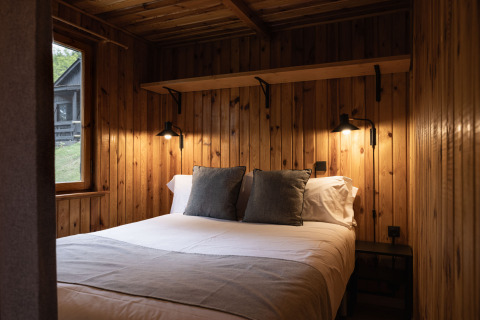 Træbeklædt glamping-hytte med dobbeltseng og bløde puder i Basecamps - Cabins Girona, set indefra.