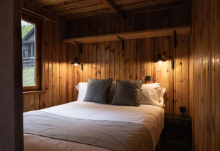 Træbeklædt glamping-hytte med dobbeltseng og bløde puder i Basecamps - Cabins Girona, set indefra.