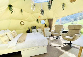 Moderne glamping dome met groot bed, comfortabele stoelen en natuurdecoratie bij Glamping Hohe Wand.