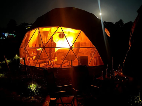 Nachtelijk beeld van een verlichte geodetische koepel bij Glamping Hohe Wand - De dome, van buitenaf gezien.