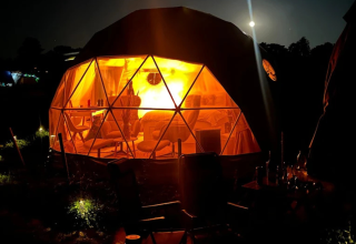 Night view of a glowing geodesic dome for glamping at Glamping Hohe Wand - De dome, captured from outside.