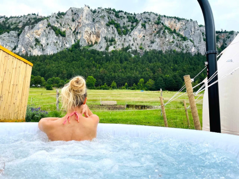 Vrouw geniet in bubbelbad met bergzicht op Glamping Hohe Wand - De dome, unieke glamping ervaring.
