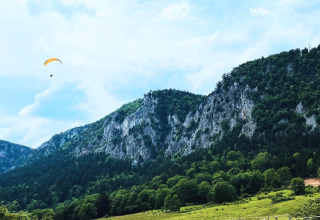 Glamping Hohe Wand - De dome : Hébergement en dôme au pied de collines vertes, parapente dans le ciel alpin.