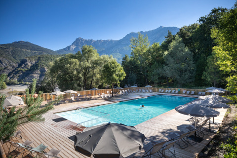 Udendørs swimmingpool med liggestole og parasoller på Camping Huttopia Lac de Serre-Ponçon, omgivet af bjerge.