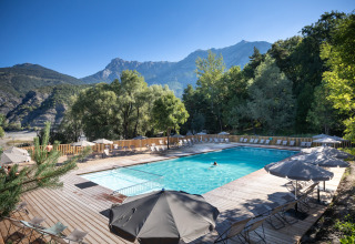 Piscina al aire libre con tumbonas y sombrillas en Camping Huttopia Lac de Serre-Ponçon, rodeada de montañas.