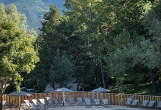 Udendørs pool med to svømmende personer, omgivet af skov og bjerge ved Camping Huttopia Lac de Serre-Ponçon.