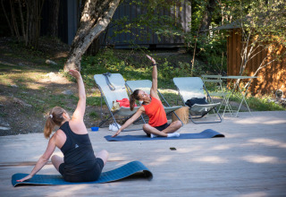 Zwei Frauen machen Yoga im Freien auf einer Holzterrasse im Camping Huttopia Lac de Serre-Ponçon im Grünen.