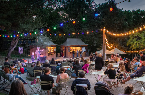 Evento nocturno al aire libre con invitados y luces en Camping Huttopia Lac de Serre-Ponçon, campamento glamping.
