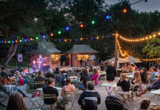 Evento nocturno al aire libre con invitados y luces en Camping Huttopia Lac de Serre-Ponçon, campamento glamping.