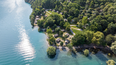 Vue aérienne du glamping Camping Huttopia Lac de Serre-Ponçon au bord d’un lac et entouré de forêt, Alpes-de-Haute-Provence.
