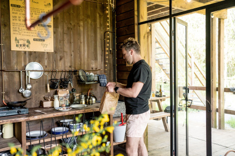 Man bereidt eten in een gezellige glampingkeuken bij Nutchel Lodges in de Ardennen, België.