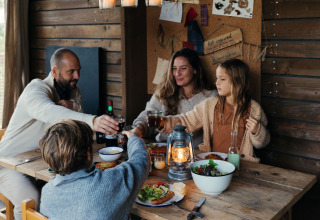 Familie nyder middag og hyggeligt samvær i træhytte på Nutchel glamping i Ardennerne, Belgien.