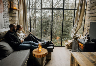 Stel ontspant zich in een Nutchel Lodge in de Ardennen, België, met uitzicht op het bos door grote ramen.