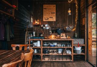Alojamiento glamping en las Ardenas, Bélgica, con interior de madera, cocina rústica y luces cálidas.