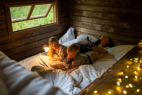 Twee kinderen lezen samen een boek in een knusse houten hut met lichtjes, Nutchel Lodges in de Ardennen.