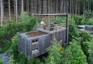 Due persone si rilassano su una terrazza di una lodge Nutchel nelle Ardenne, Belgio, circondati dalla foresta.