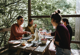 Vier mensen ontbijten samen buiten aan een houten tafel bij Nutchel - Lodges in de Ardennen, België.